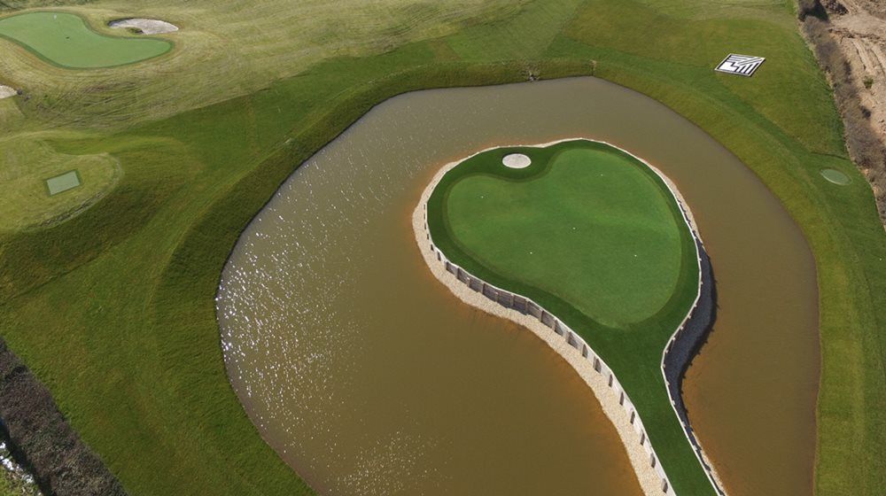 Charlotte Aerial view of a vibrant green synthetic grass island in a natural pond on a golf course